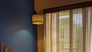 A bedroom with a bed, a wicker headboard, a hanging light fixture, and a window with blinds. - Seneh Homes - An Assamese homestay experience with WiFi, Views, & AC in Guwahati (Guwahati)