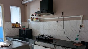 A kitchen with a gas stove, a black range hood, and a vent. There are cabinets and a countertop. - Seneh Homes - An Assamese homestay experience with WiFi, Views, & AC in Guwahati (Guwahati)