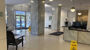 Un hall d’hôtel avec des colonnes en marbre, un comptoir d’accueil et un banc noir.