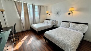 Une chambre d’hôtel avec deux lits, un bureau, une chaise et une lampe fixée au mur.