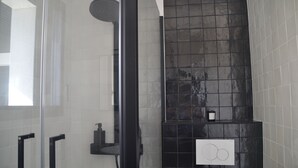 Une salle de bain moderne dotée d’une douche à parois de verre, d’un mur recouvert de carreaux noirs et d’un panneau de commande blanc.