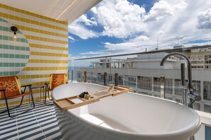 Un baño moderno con una bañera independiente, una silla de madera y una mesa de vidrio con una bandeja.