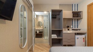 A modern hotel room with a bed, a TV mounted on the wall, a kitchenette with a microwave, and a bathroom visible through an open door. - Refuge a few steps from Copacabana Beach | Q10 PCD (Rio de Janeiro)