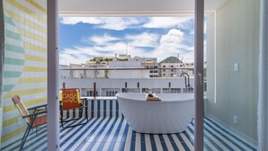 A modern bathroom with a bathtub, a chair, and a view of the cityscape through a glass door.