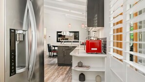 Une cuisine moderne avec un réfrigérateur en acier inoxydable, une machine à café rouge et un îlot central blanc.