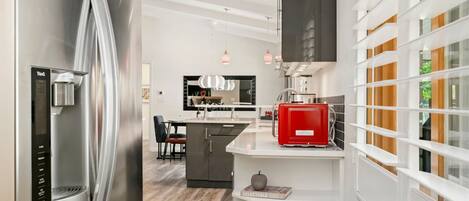 A modern kitchen with a stainless steel refrigerator, a red coffee machine, and a white island.