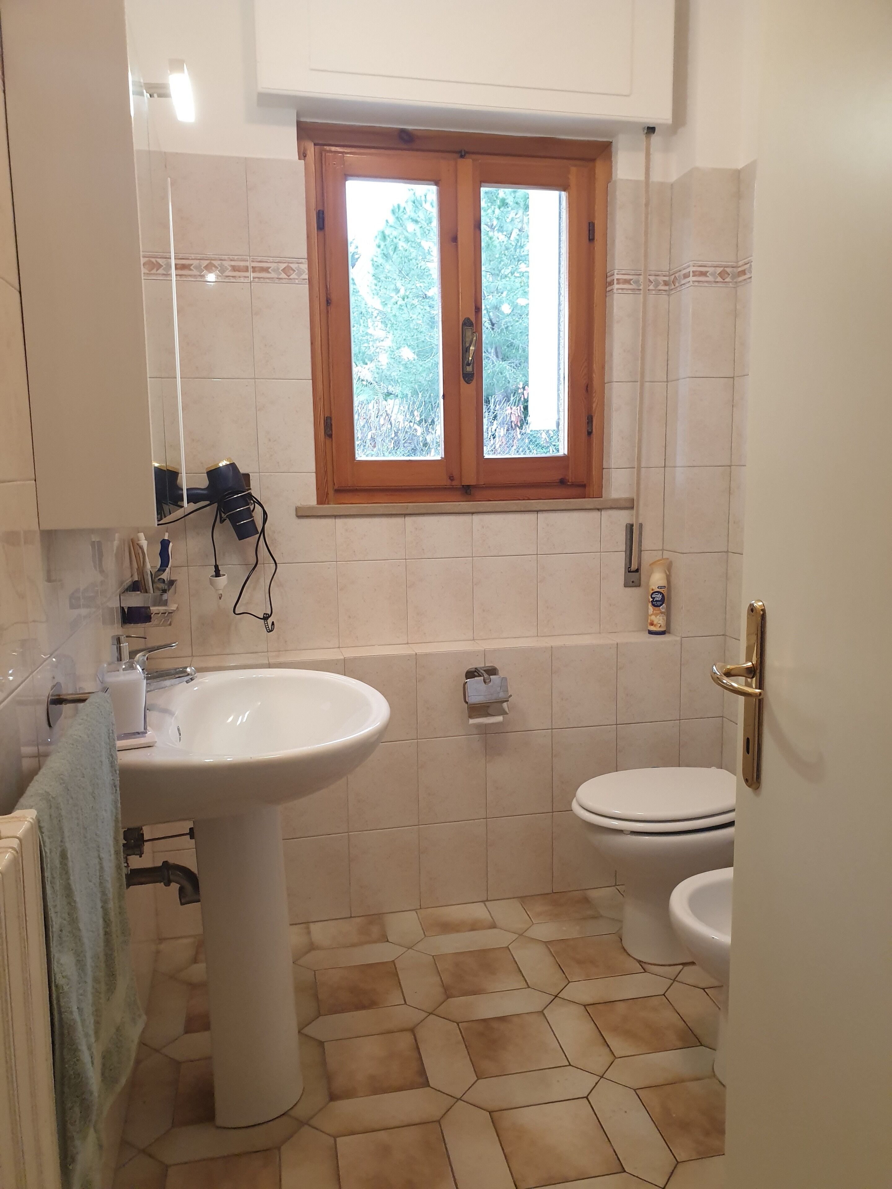 Une salle de bain équipée d’un lavabo, de toilettes et d’une fenêtre donnant sur des arbres.