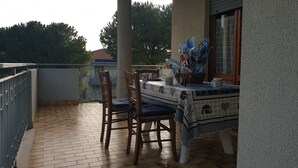 En balkon med et bord dækket til to, med en mønstret dug og en kurv med genstande.