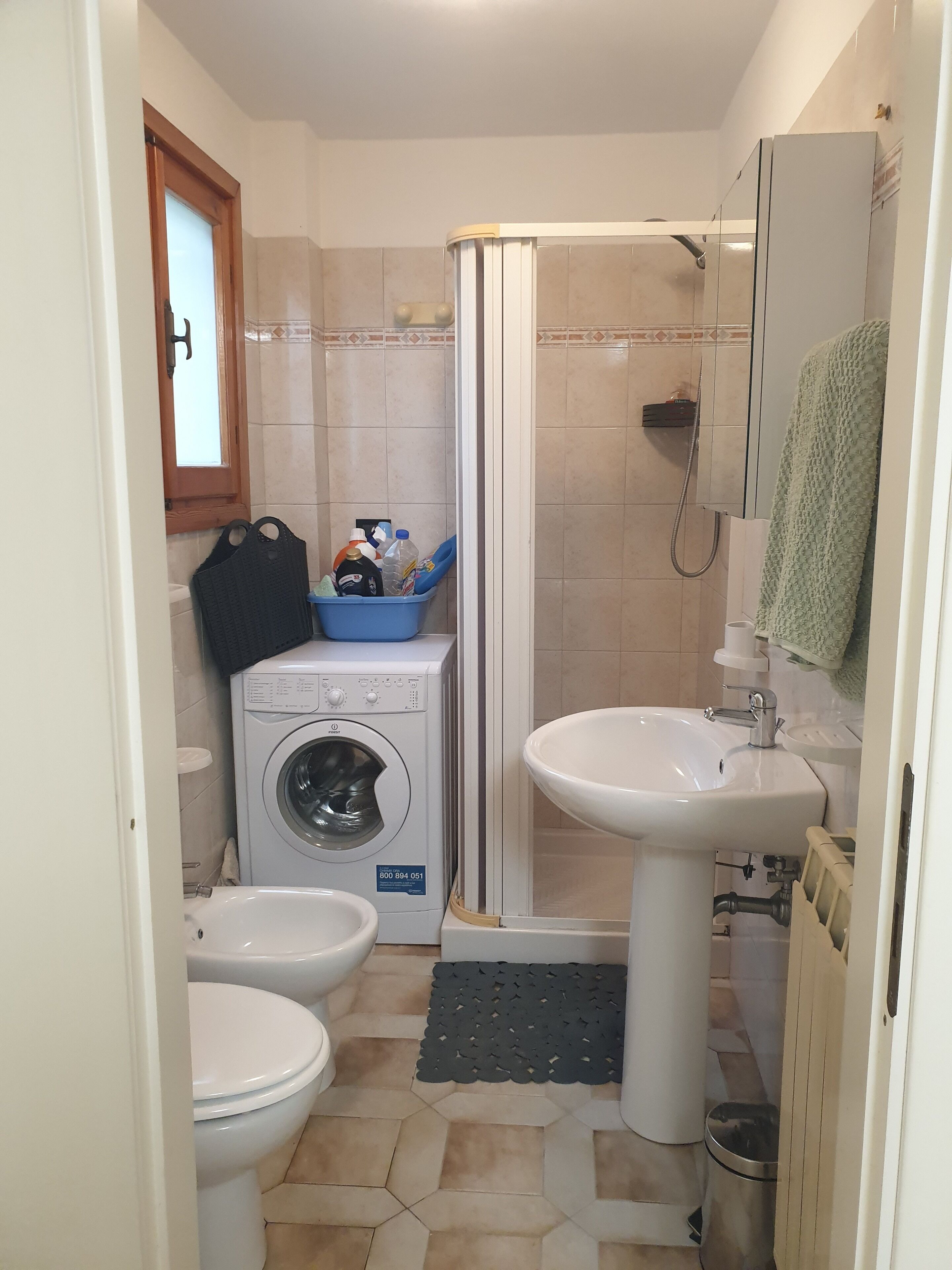 Ein kleines Badezimmer mit Waschmaschine, zwei Toiletten, einer Dusche und einem Waschbecken.