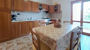 A kitchen with wooden cabinets, a tiled backsplash, a dining table with chairs, and a view through a glass door.