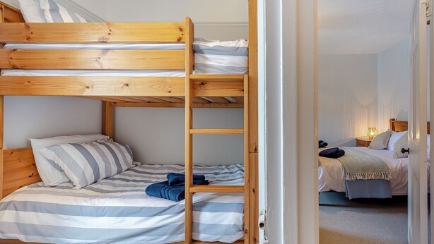 Ein Schlafzimmer mit Stockbett, einer Holzleiter, gestreifter Bettwäsche und einem Nachttisch mit Lampe.