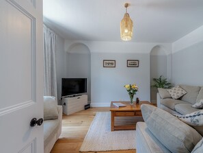 Ein Wohnzimmer mit Fernseher, Sofas, einem Couchtisch und einer Pendelleuchte.