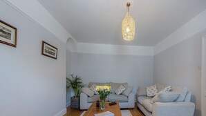 Ein Wohnzimmer mit Couchtisch aus Holz, zwei grauen Sofas, einer Pendelleuchte und einem gerahmten Bild an der Wand.