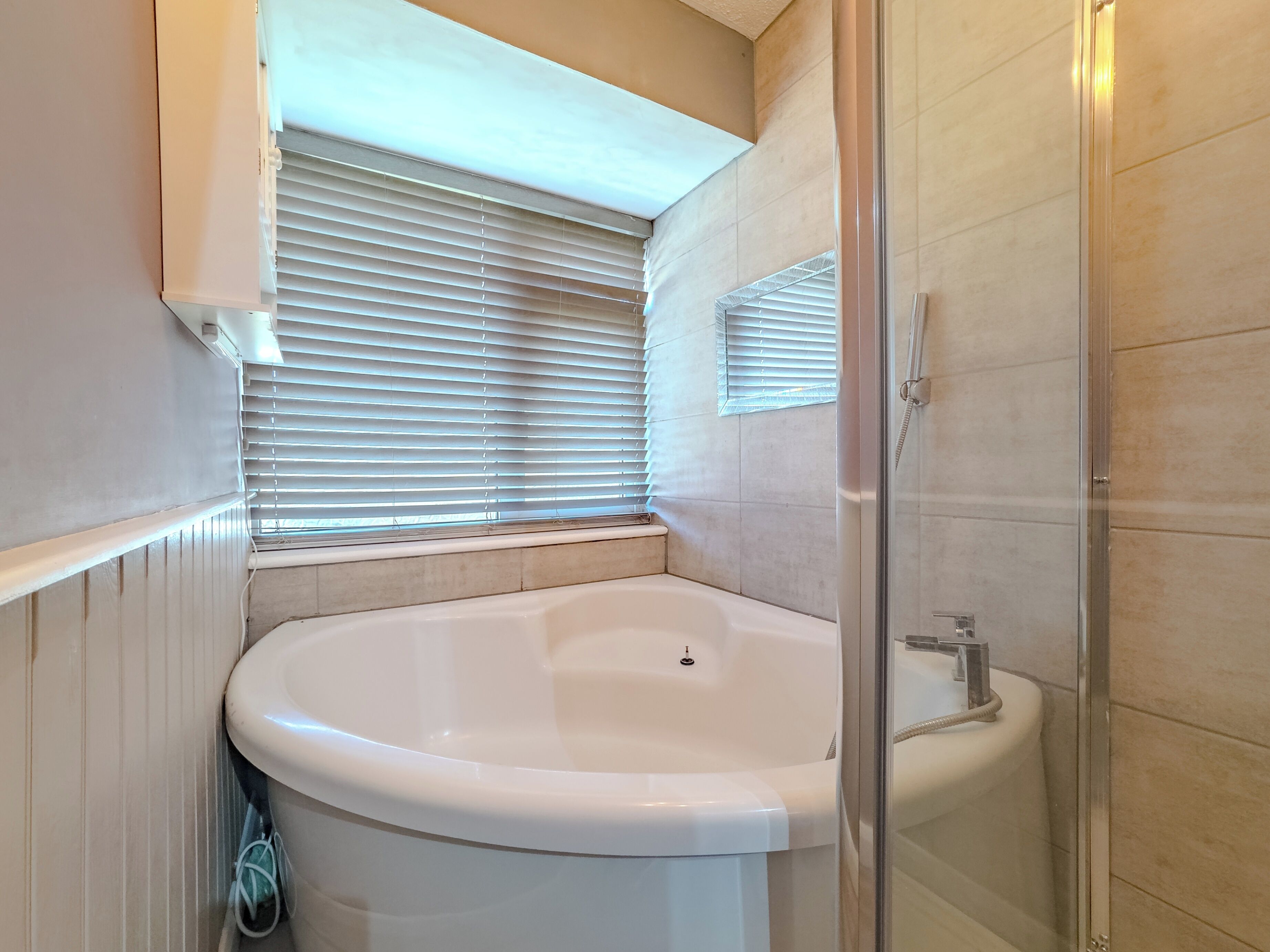 A bathroom with a freestanding bathtub, a glass-enclosed shower, and a window with blinds.