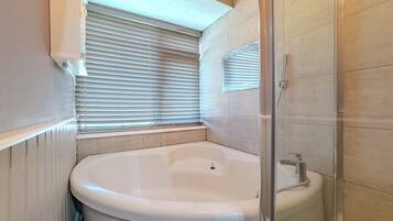 A bathroom with a freestanding bathtub, a glass-enclosed shower, and a window with blinds.