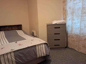 Een slaapkamer met een bed, een dressoir en een raam met gordijnen.