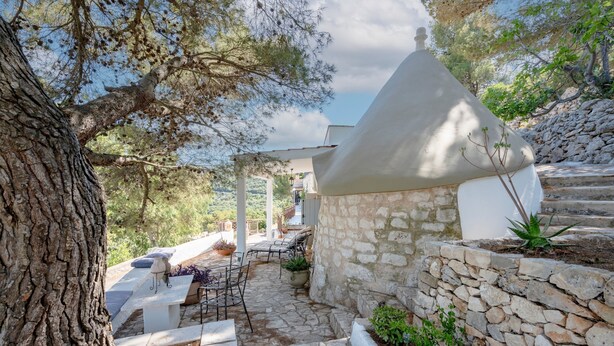 Una casa de piedra con techo cónico, una escalera de piedra y zona de estar al aire libre.