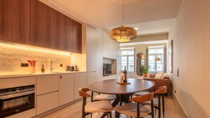 A modern kitchen with a built-in oven, a dining area with a round table and chairs, and a large window providing natural light.