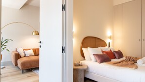 A modern bedroom with a bed, bedside table, and a sofa in a bright, minimalist style.