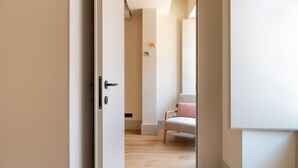A modern bedroom with a wooden floor, a white bed, and a chair with a pink cushion.