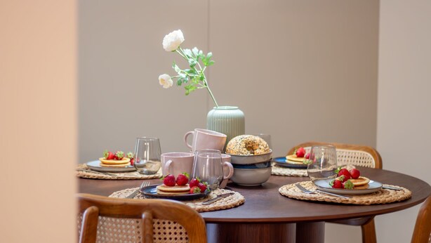 A round dining table with placemats, plates with strawberries, a pitcher, and a vase with a flower.