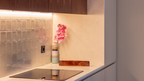Un baño con pared de azulejos, un espejo, un florero con flores rosas y un jabonera.
