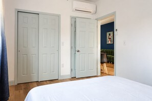 A bedroom with a bed, two doors, an air conditioning unit, and a green sofa in the adjacent room.