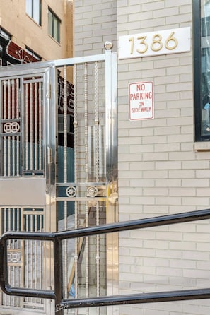 A building entrance with a metal gate, a 'No Parking on Sidewalk' sign, and the address '1386' on the wall.