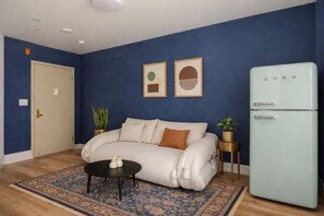 A living room with a sofa, a small table, a refrigerator, and two framed pictures on the wall.