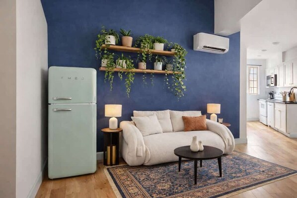 A living room with a blue accent wall, a retro-style refrigerator, a sofa with cushions, a coffee table, and a patterned rug.