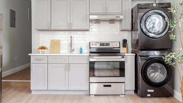 A modern kitchen with grey cabinets, a stainless steel oven, a built-in microwave, and a stacked washer and dryer.
