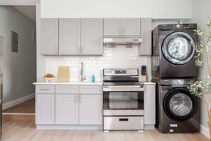 Een moderne keuken met grijze kastjes, een roestvrijstalen oven, een inbouwmagnetron, en een stapel wasmachine en droger.