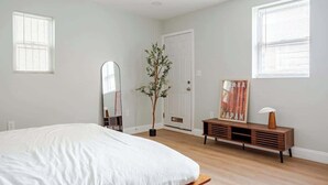 A bedroom with a large bed, a wooden dresser, a mirror, and a door.