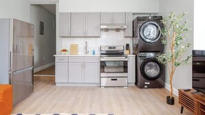 A modern kitchen with stainless steel appliances, a built-in oven, a washing machine, and a potted plant.