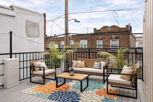 A balcony with wicker furniture, a patterned rug, and a view of a brick building.