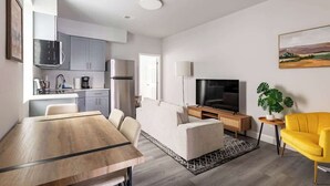 En modern lägenhet med matplats, soffa, TV och kök.