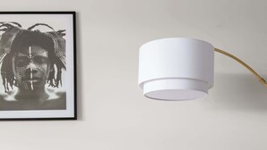Um sofá branco com várias almofadas, um quadro na parede e um candeeiro de chão branco com base dourada.