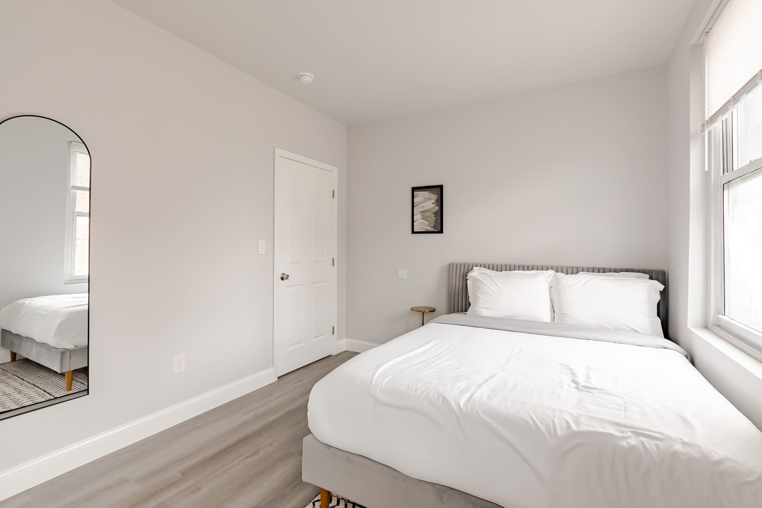 A bedroom with a bed, a door, a small table, and a window.