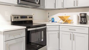 Uma cozinha moderna com armários cinza, fogão de aço inoxidável, micro-ondas e cafeteira.