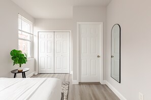 Quarto com cama, planta em vaso, porta branca e espelho.