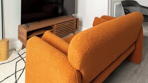Ein modernes Wohnzimmer mit einem großen Flachbildfernseher, einer Holzunterhaltungsecke und einem leuchtend orangefarbenen Sofa.