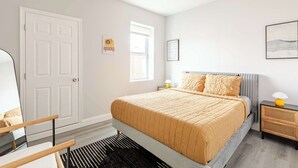 Ein Schlafzimmer mit Bett, Stuhl, Nachttisch, Lampe und Tür.
