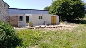 A rustic building with a stone wall, a wooden door, and a small patio area with a table and chairs. - Holiday Home 'Glycine' in Paimpol with Private Kitchen, Air Conditioning, and Bike Storage (Paimpol)