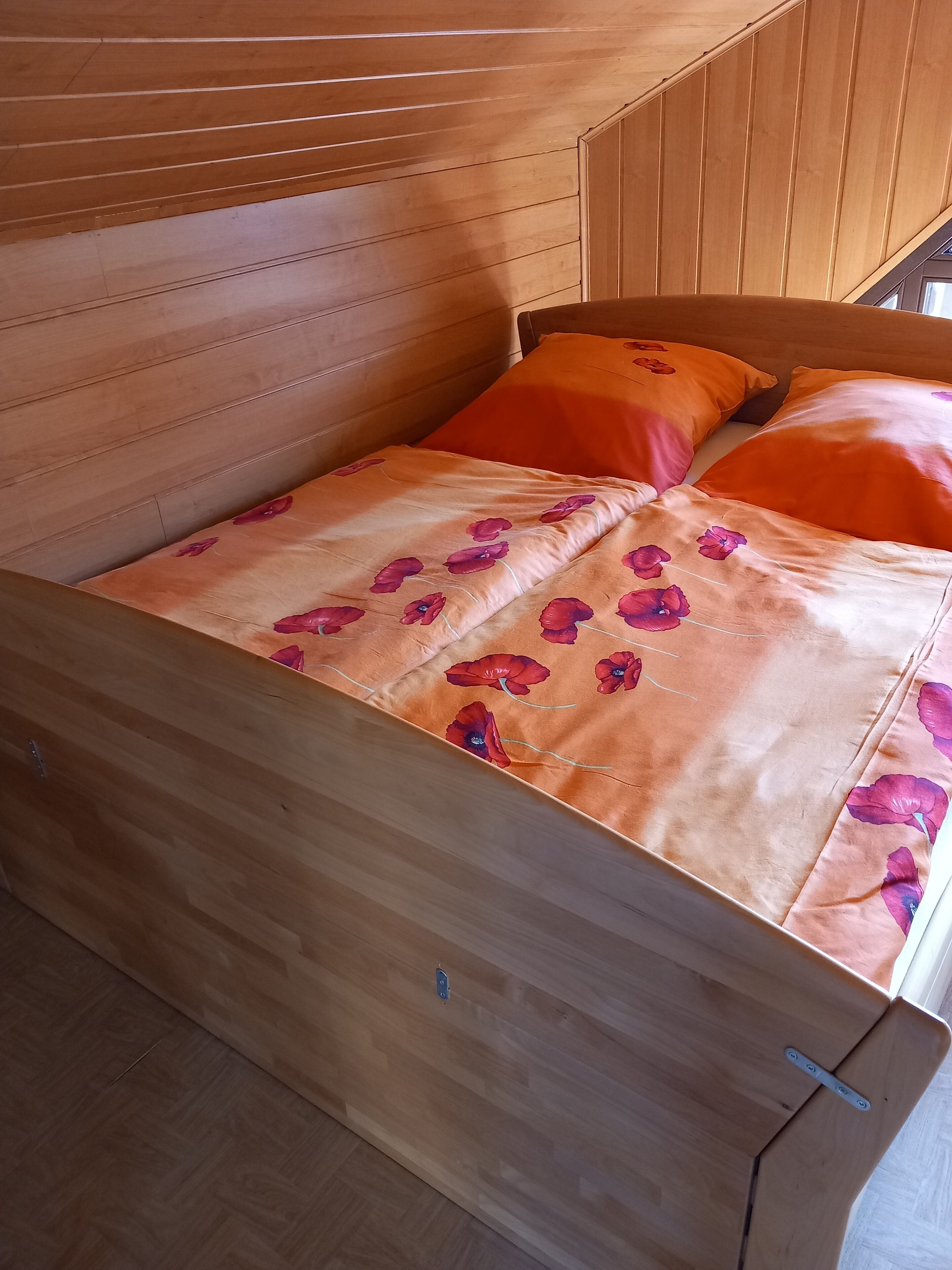 En säng i trä med orange och rosa blommönstrat sängkläder.
