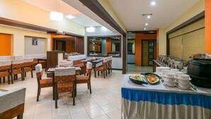 A dining area with tables and chairs, a buffet line with dishes, and a large pot on the right. - Harithagiri Hotel (Kalpetta)