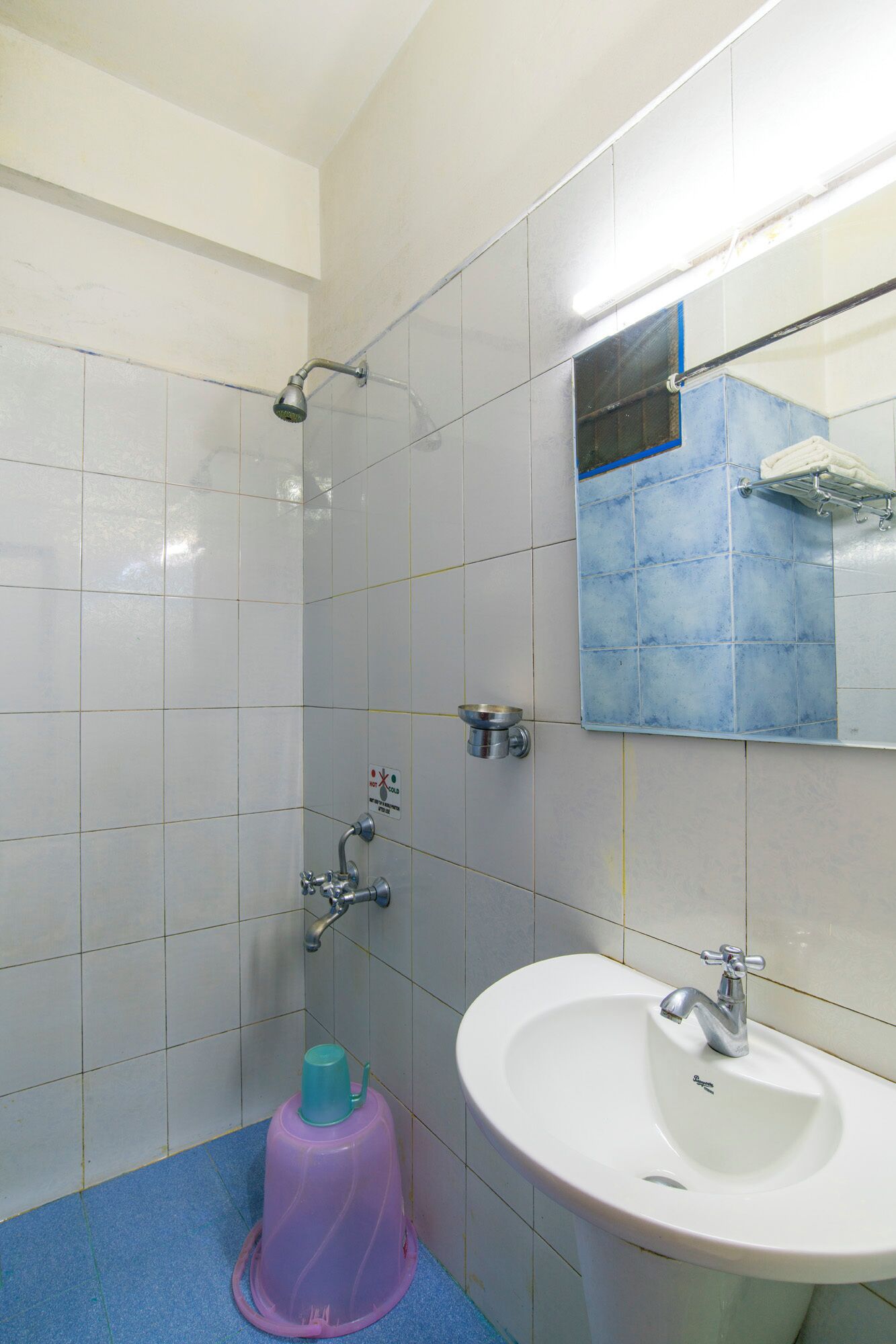 A bathroom with white and blue tiles, a shower, a sink, and a mirror.