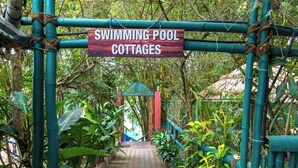 A sign for 'Swimming Pool Cottages' with a pathway leading to a gated entrance surrounded by lush greenery. - Harithagiri Hotel (Kalpetta)