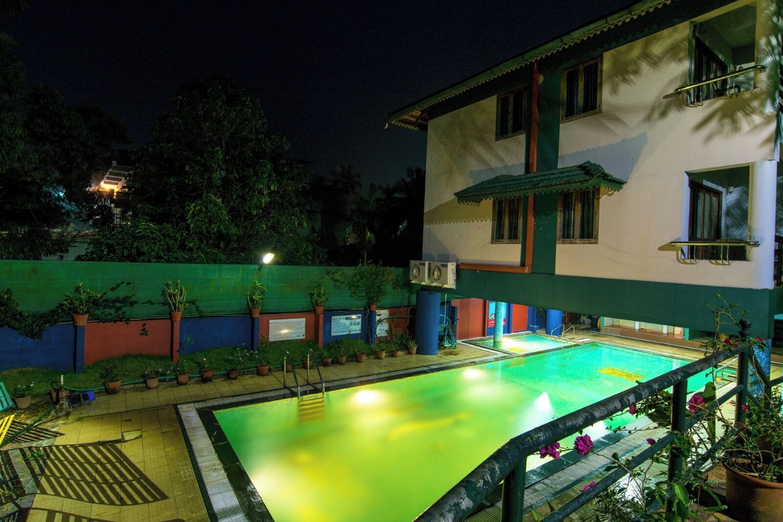 A swimming pool with a greenish hue, surrounded by a low wall with potted plants.