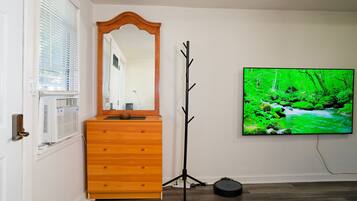 A room with a wooden dresser, a mirror, a coat rack, and a large TV displaying a green landscape.