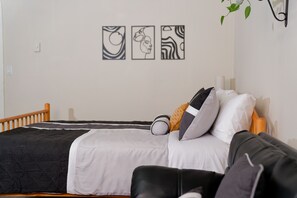 A neatly made bed with a black and white duvet, a wooden headboard, and a bedside table with a lamp. There are three framed artworks on the wall above the bed. - 'Croton Nook' - Spacious Studio with Full Eat-in Kitchen, Cozy Getaway (Croton-on-Hudson)